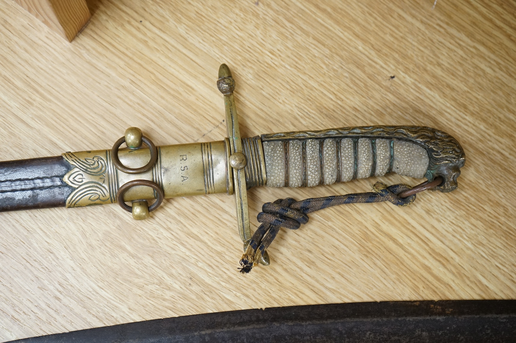 A post 1902 Naval Officer’s Dirk, the regulation blade with crowned fouled anchor, regulation hilt with remains of bullion dress knot in its leather scabbard with brass mounts, locket engraved with owners initials; RSA